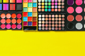 Face paints and makeup products on yellow background, top view. Space for text