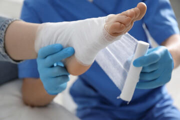 Doctor bandaging patient's foot in clinic, closeup