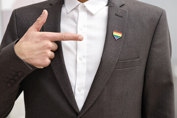Man pointing at heart shaped pin in colors of LGBT flag indoors, closeup