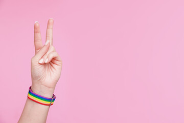 Woman wearing wristband in LGBT colors and showing peace sign on pink background, closeup. Space...