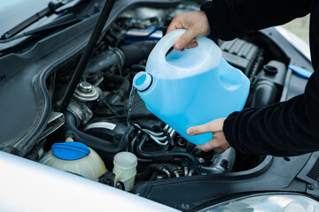 Man pouring windshield washer from plastic canister into car reservoir, closeup
