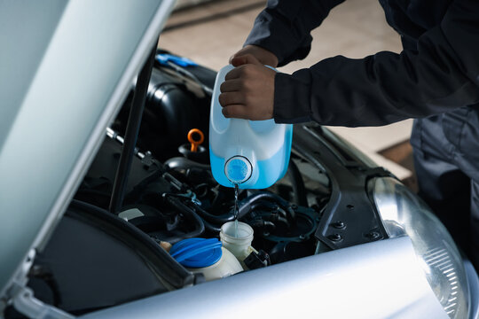 Man pouring windshield washer from plastic canister into car reservoir outdoors, closeup