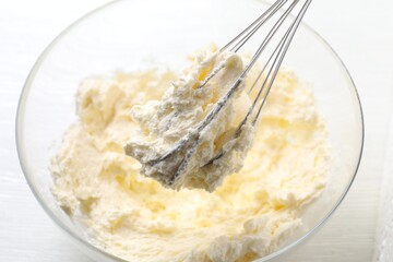 Bowl with whisk and whipped cream on white wooden table, closeup