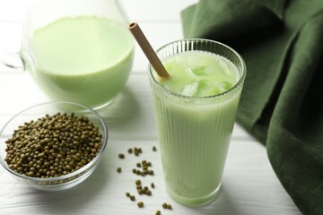Fresh mung bean juice with ice in glass and seeds on white wooden table, closeup