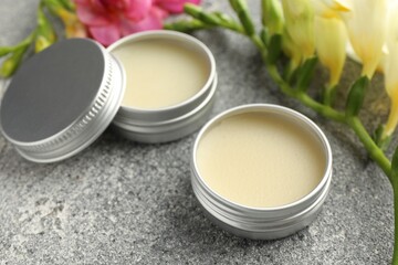Moisturizing lip balms and beautiful flowers on grey textured table, closeup