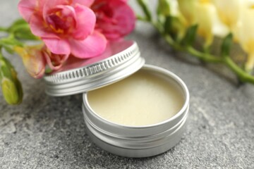 Moisturizing lip balm and beautiful flowers on grey textured table, closeup