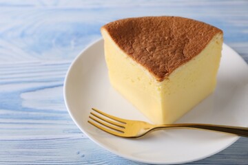 Piece of tasty Japanese Castella sponge cake and fork on light blue wooden table, closeup. Space for text