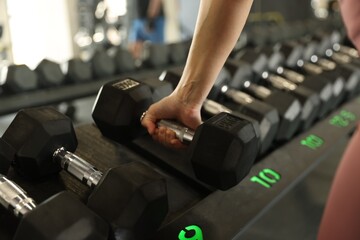 Woman taking rubber hex dumbbell in gym, closeup