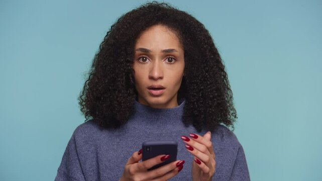 Shocked woman reading unexpected news on smartphone on blue background