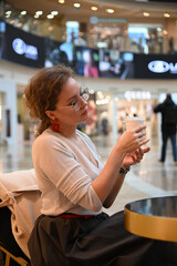 A young woman in a cafe in a shopping center drinks coffee at a table