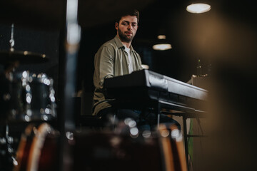 A musician playing a keyboard with a focused expression, surrounded by drum sets in a professional music studio with creative lighting.