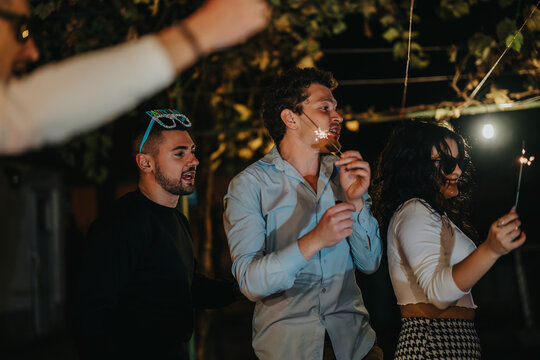 A joyful scene capturing friends holding sparklers during an evening celebration under lights outdoors.