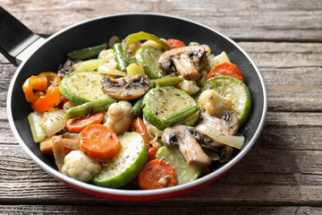 Different vegetables and mushrooms in frying pan on wooden table, closeup