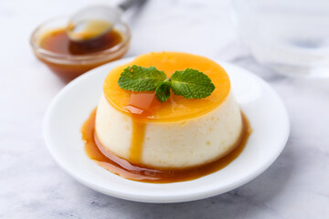 Tasty pudding with caramel sauce served on white marble table, closeup
