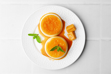 Tasty puddings with caramel sauce served on white tiled table, top view