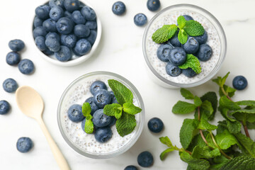Delicious chia pudding with blueberries and mint in glasses on white table, flat lay