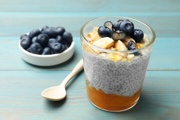 Delicious chia pudding with blueberries, banana and oatmeal in glass served on light blue wooden table, closeup