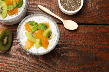 Delicious chia pudding with kiwi, peach and mint in glasses served on wooden table, flat lay. Space for text