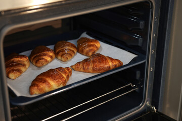 Freshly baked croissants on baking sheet in oven, closeup