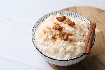 Delicious rice pudding with cinnamon and cashew nuts on white tiled table, closeup