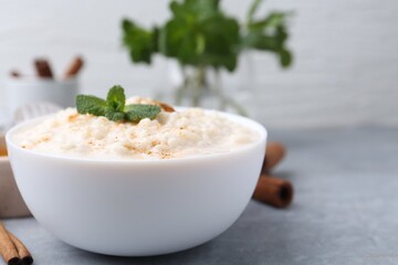 Tasty rice pudding with cinnamon and mint on light grey table, closeup. Space for text