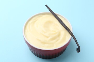 Tasty vanilla pudding and pod on light blue background, closeup