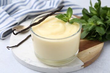 Tasty vanilla pudding, mint and pods on light grey table, closeup