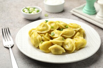Tasty dumplings with green onion and fork on grey textured table, closeup