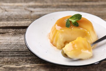Delicious pudding with caramel sauce and mint served on wooden table, closeup