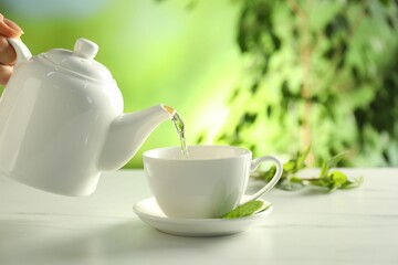Woman pouring freshly brewed tea from teapot into cup at white marble table outdoors, closeup