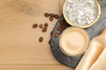 Coffee cream liqueur in glass, ice and beans on wooden table, flat lay. Space for text