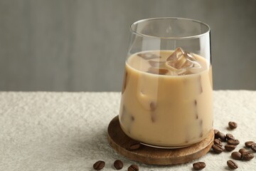 Coffee cream liqueur in glass and beans on white textured table, closeup. Space for text