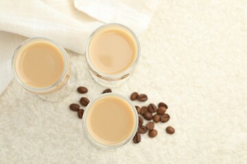 Coffee cream liqueur in glasses and beans on white textured table, flat lay. Space for text