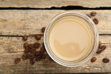 Coffee cream liqueur in glass and beans on wooden table, flat lay. Space for text