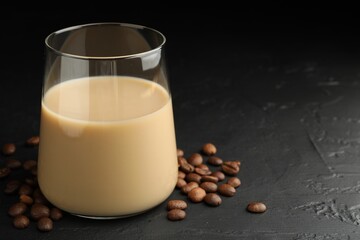 Coffee cream liqueur in glass and beans on black table, closeup. Space for text