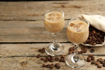 Coffee cream liqueur in glasses and beans on wooden table, closeup. Space for text