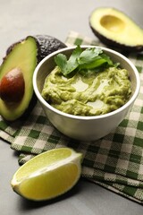 Tasty avocado dip in bowl, parsley and fruits on grey table, closeup
