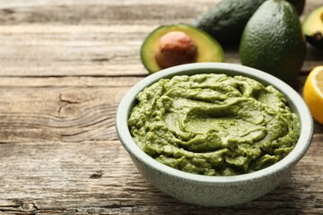 Tasty avocado dip in bowl and fruits on wooden table, closeup. Space for text