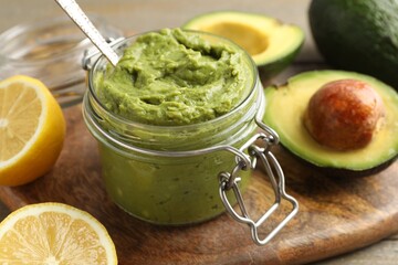 Tasty avocado dip in glass jar and fruits on table, closeup
