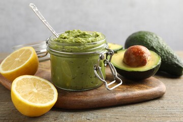 Tasty avocado dip in glass jar and fruits on wooden table, closeup