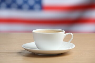 Cup of coffee on wooden table against American flag