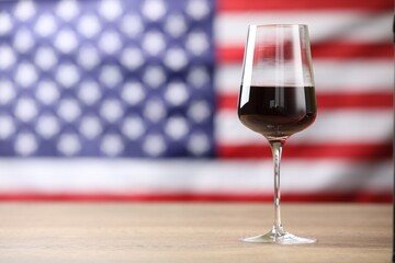 Glass of wine on wooden table against American flag. Space for text