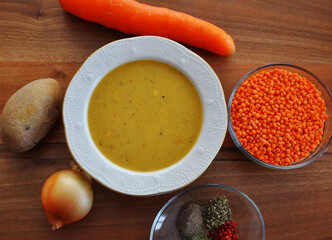 A bowl red lentil soup and ingredient (potato, onion, carrot, red lentil, spices)