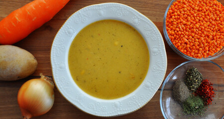 A bowl red lentil soup and ingredient (potato, onion, carrot, red lentil, spices)