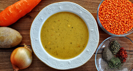 A bowl red lentil soup and ingredient (potato, onion, carrot, red lentil, spices).