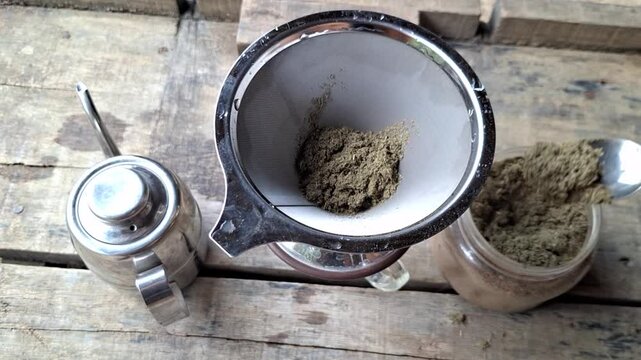 Green kratom leaf powder (Mitragyna speciosa) being brewed using a stainless steel strainer. The herbal drink is known for its traditional use in some cultures