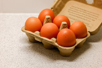 Six brown eggs with speckled shells in cardboard carton on kitchen counter, ready for cooking.