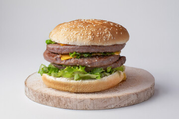 Triple meat burger, melted cheese and fresh lettuce, served on a wooden cutting board. Horizontal photo with natural light, perfect for food, fast food and American cuisine themes.