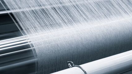 A piece of fabric is being woven on a loom. fabric is made of a silky material and is being woven...