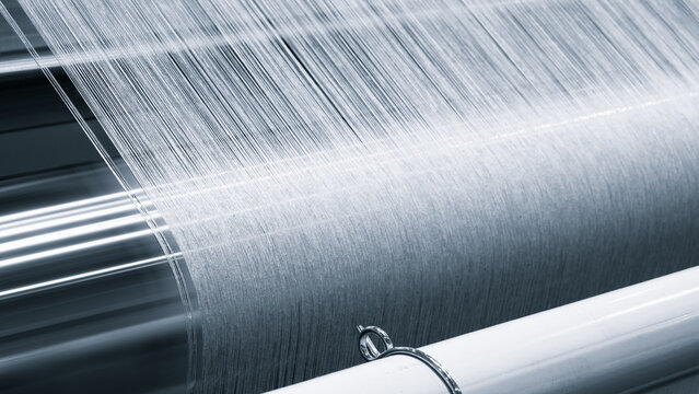 A piece of fabric is being woven on a loom. fabric is made of a silky material and is being woven in a pattern. loom is a large, industrial machine that is used to create textiles